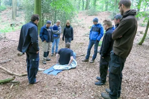 Gruppe steht um eine Person, die auf einer Decke im Wald sitzt