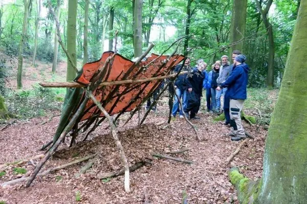 Gruppe steht vor einer Tarp-Notunterkunft aus Ästen und einer Plane im Wald