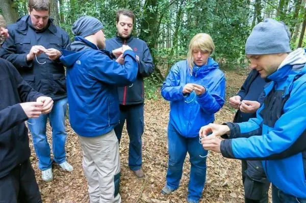 Gruppe von Personen übt Knotenbinden im Wald beim Survival Training