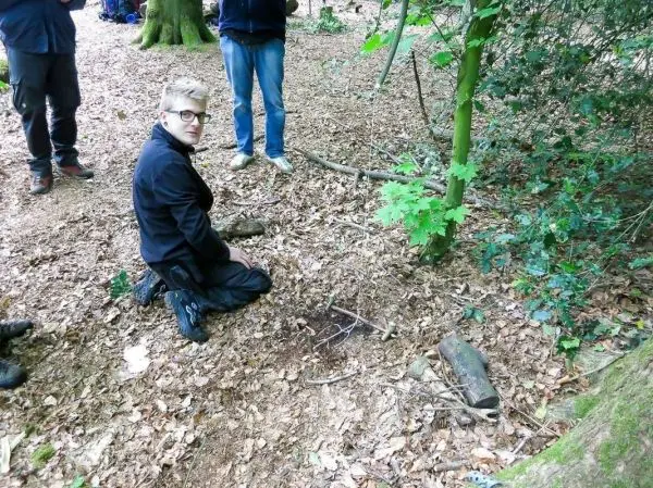 Knieende Person arbeitet an einer kleinen Konstruktion aus Ästen im Laub