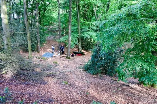 Lagerplatz im Wald mit Tarp-Notunterkunft und mehreren Personen