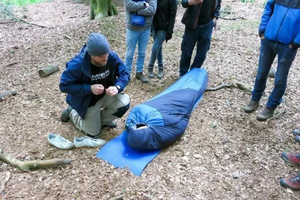 Mann knüpft eine improvisierte Trage aus einem Schlafsack auf dem Waldboden