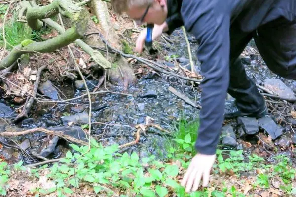 Person balanciert über einen kleinen Bach, Hände zur Stabilisierung ausgestreckt
