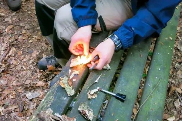 Person entzündet Feuer mit Zunder auf Holzbank beim Survival Training