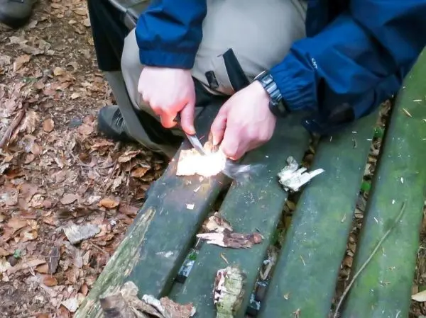 Person entzündet mit einem Feuerstahl Holzstück auf einer Bank beim Survival Training