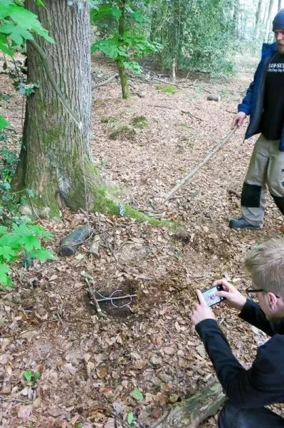 Person fotografiert eine selbstgebaute Falle im Wald