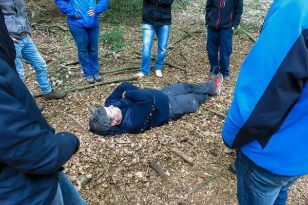 Person liegt auf dem Boden im Laub, umgeben von mehreren Personen