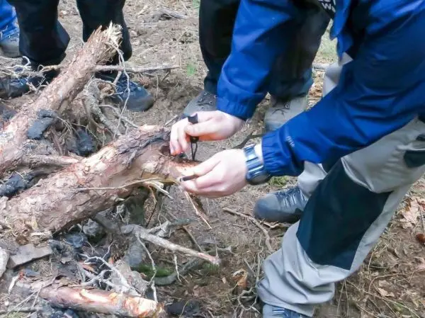 Person schnitzt mit einem Messer an einem Baumstamm beim Überlebenstraining