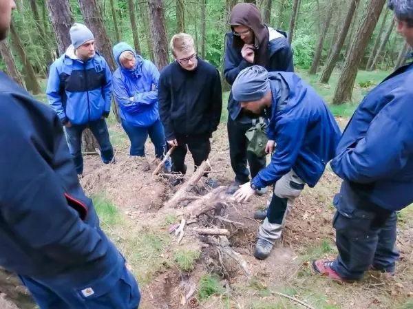 Person zeigt Gruppe Holzstruktur im Wald beim Überlebenstraining