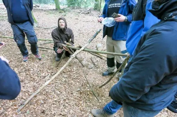 Selbstgebaute Konstruktion aus Ästen im Wald, umgeben von mehreren Personen