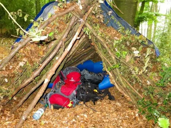 Tarp-Notunterkunft aus Ästen und Blättern mit Rucksäcken im Inneren