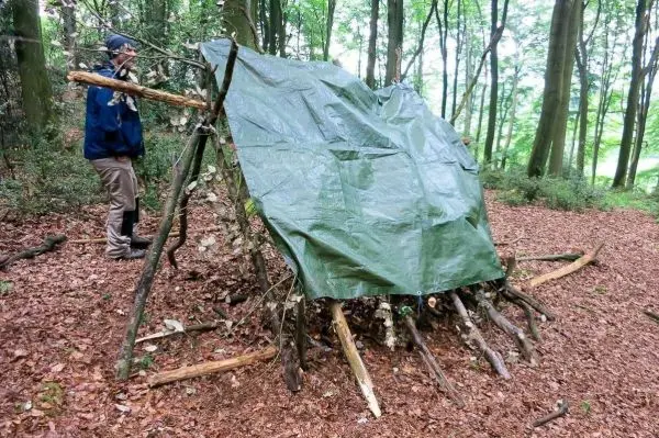 Tarp-Notunterkunft aus Ästen und einer Plane im Wald