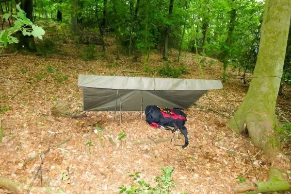 Tarp-Notunterkunft mit Rucksack unter einem Baum im Wald