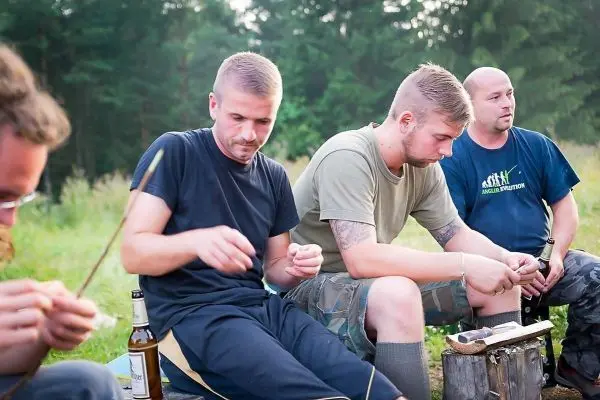 Drei Personen sitzen am Boden und bearbeiten Holzstücke mit Werkzeug