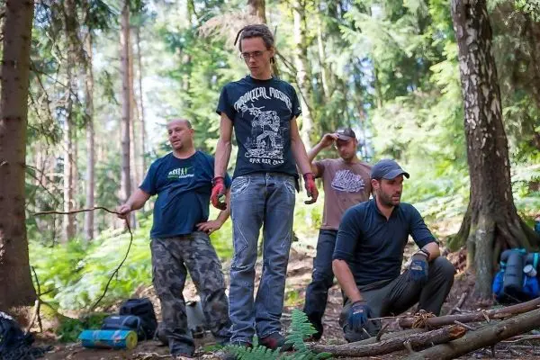Gruppe arbeitet im Wald an einer Holzstruktur mit verschiedenen Werkzeugen