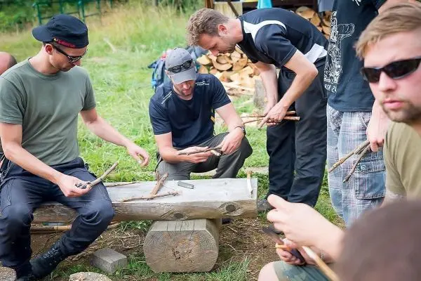 Gruppe von Personen bearbeitet Holzstücke an einem Tisch beim Überlebenstraining