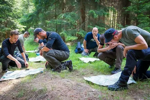Gruppenteilnehmer analysieren Karten im Wald, kniend auf dem Boden