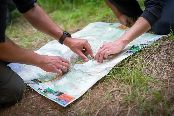 Hände zeigen auf eine Landkarte im Gras beim Überlebenstraining