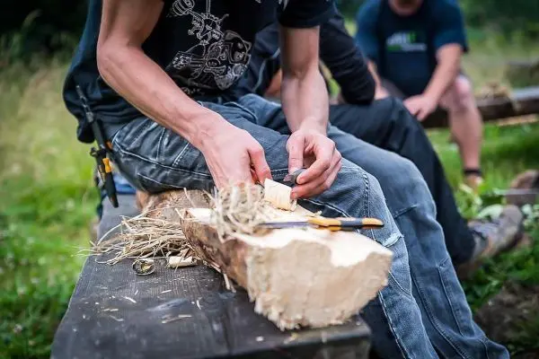 Holzstück wird mit einem Messer bearbeitet, Zunder liegt daneben