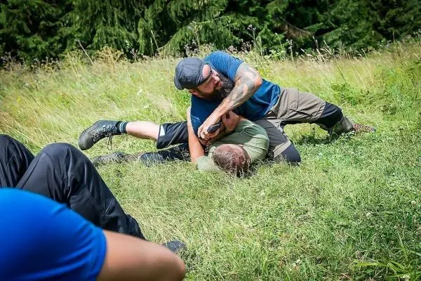 Kämpfer übt Bodenkampf-Technik auf einer Wiese mit Gras