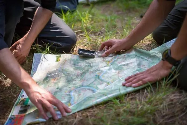 Karte liegt auf dem Boden, Kompass und Lupe werden zur Orientierung genutzt