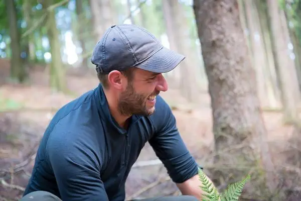 Lächelnder Mann sitzt im Wald und betrachtet einen Farn
