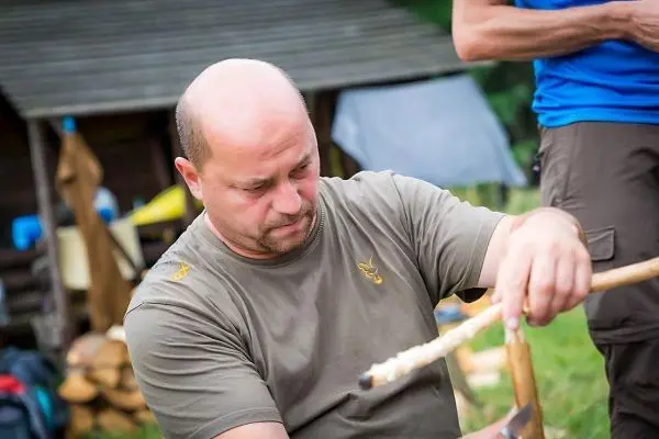 Mann bearbeitet einen Holzstock mit einem Messer in einer natürlichen Umgebung