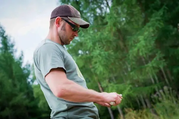 Mann hält ein Messer und bearbeitet einen Holzstock im Wald