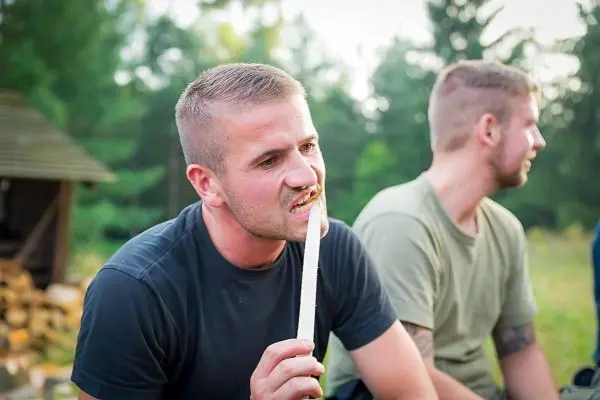 Mann hält einen langen Stock im Mund und sitzt neben einem anderen Mann