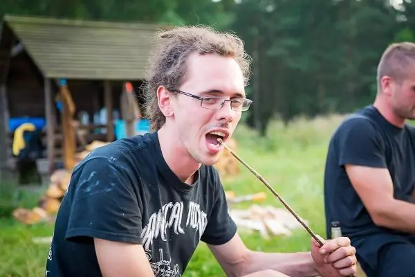 Mann hält einen Stock im Mund und sitzt neben einem anderen Mann