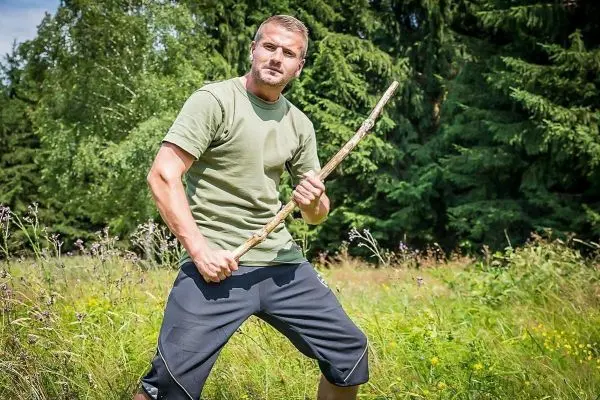 Mann hält einen Stock in einer aufrechten Position in einer Wiese