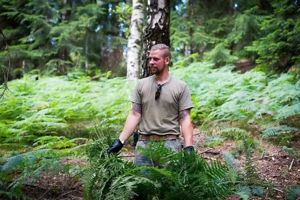 Mann hält Farnblätter in einem Waldgebiet