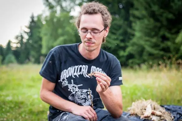 Mann hält Zunder in der Hand und sitzt auf einer Decke im Freien