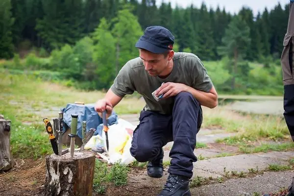 Mann kniet neben einem Baumstumpf und bearbeitet ein Messer