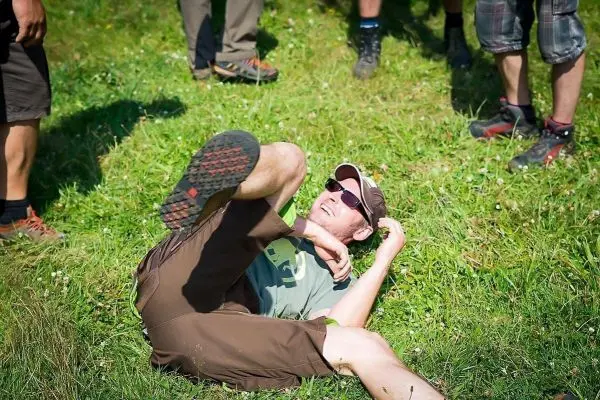 Mann liegt auf dem Gras und lacht, während andere Personen um ihn stehen