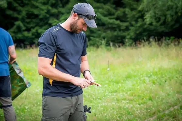 Mann schnitzt mit einem Messer an einem Holzstück im Freien