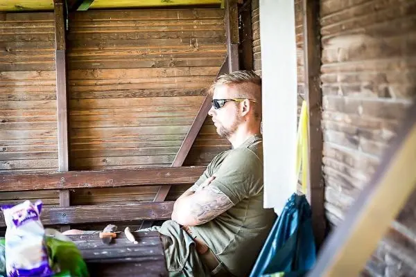 Mann sitzt mit verschränkten Armen auf einer Holzbank in einer Hütte