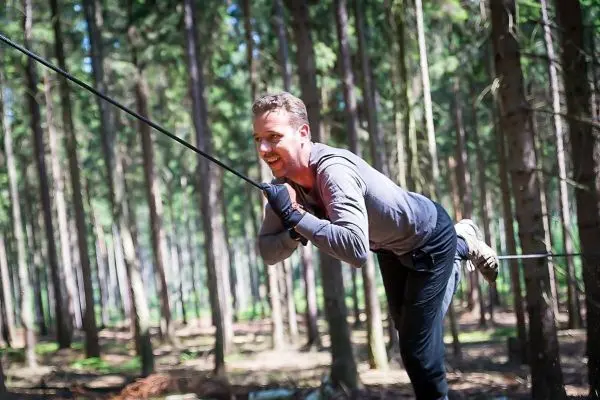 Mann überquert selbstgebaute Seilbrücke zwischen Bäumen im Wald