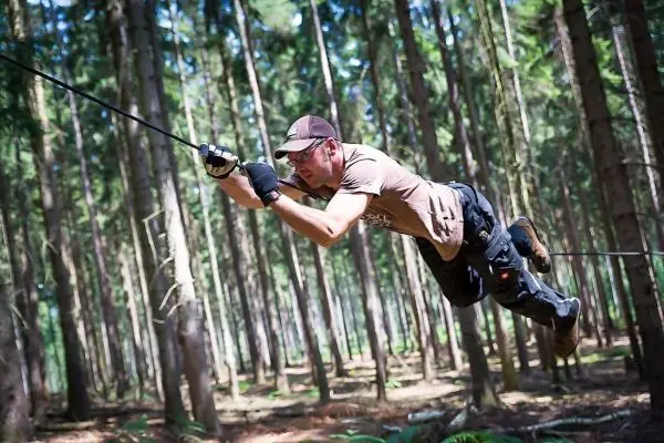 Mann überquert selbstgebaute Seilbrücke zwischen Bäumen im Wald