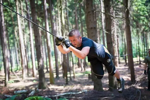Mann überquert selbstgebaute Seilbrücke zwischen Bäumen im Wald