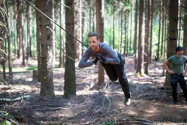 Mann überquert selbstgebaute Seilbrücke zwischen Bäumen im Wald