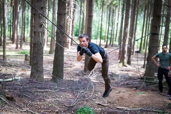 Mann überquert selbstgebaute Seilbrücke zwischen Bäumen im Wald