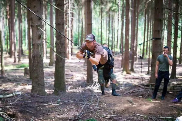Mann überquert selbstgebaute Seilbrücke zwischen Bäumen im Wald