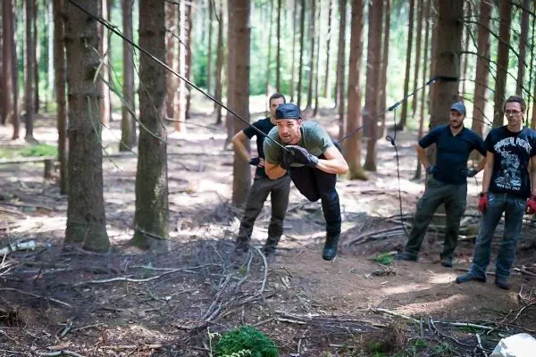 Mann überquert selbstgebaute Seilbrücke zwischen Bäumen im Wald