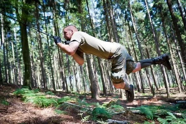 Mann überquert selbstgebaute Seilbrücke zwischen Bäumen im Wald