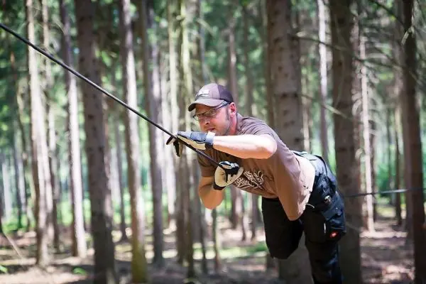 Mann überquert selbstgebaute Seilbrücke zwischen Bäumen im Wald