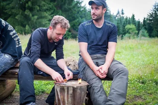 Mann zündet Zunder auf einem Baumstumpf an, während ein anderer zuschaut