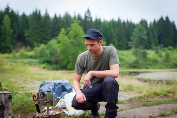 Messer stehen auf einem Baumstumpf, während ein Mann kniet und sie betrachtet
