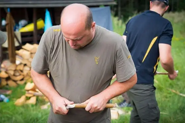 Person schnitzt mit einem Messer an einem Stock beim Überlebenstraining