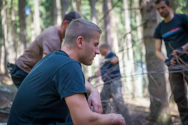Person sitzt im Wald und beobachtet andere Personen beim Arbeiten